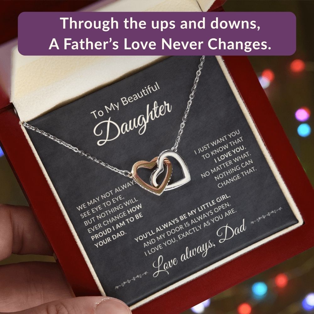 Promotional graphic featuring an open mahogany-style gift box with an interlocking hearts necklace and message card reading: Through the ups and downs, a father's love never changes.