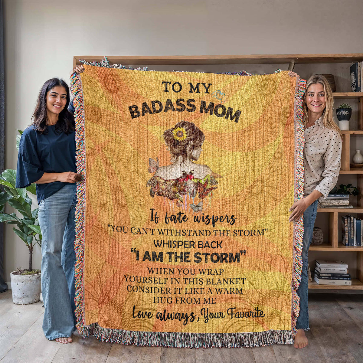 Personalized wooven blanket with sunflower design and "To My Badass Mom" message. Held up by 2 women 
