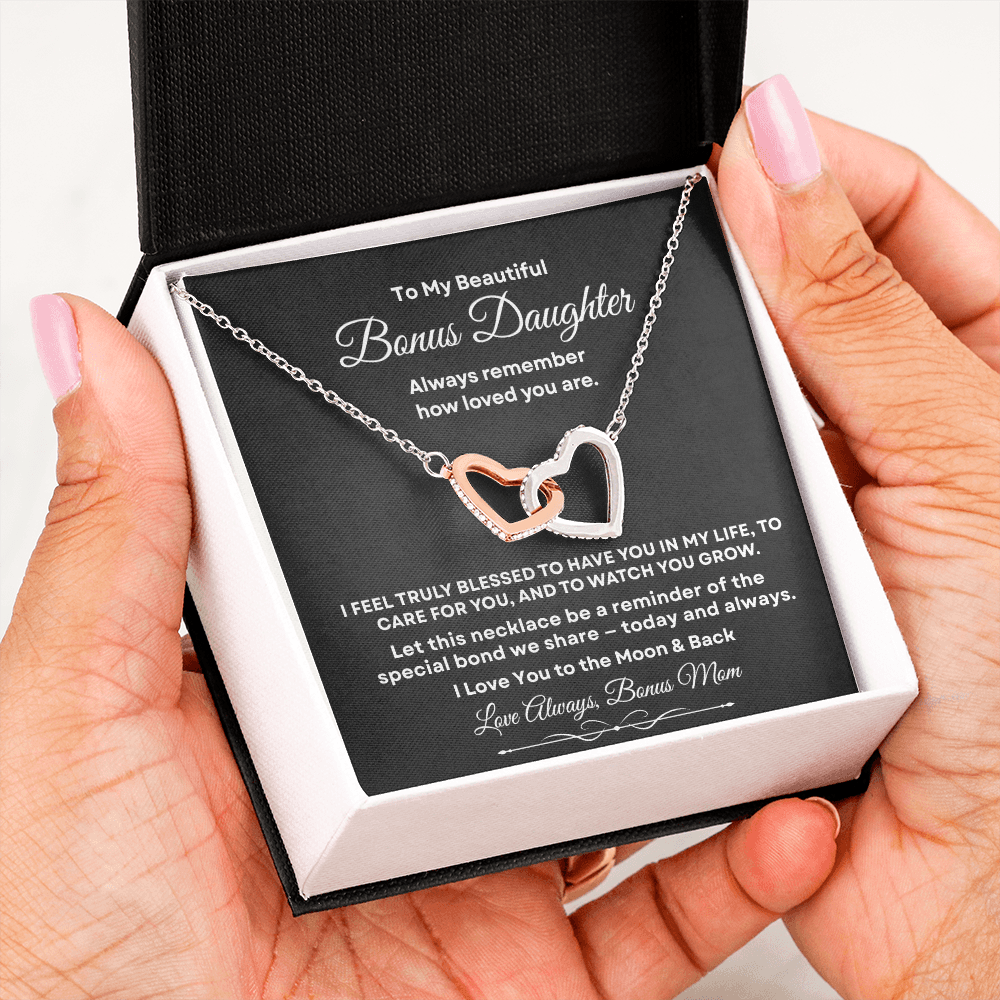 Hands holding an open black standard gift box displaying the interlocking hearts necklace and message card for bonus daughter.