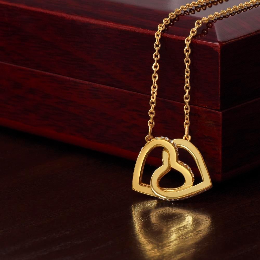 Close-up of the 18k yellow gold finish interlocking hearts necklace resting in front of a mahogany-style luxury box, showcasing the pavé cubic zirconia crystals.
