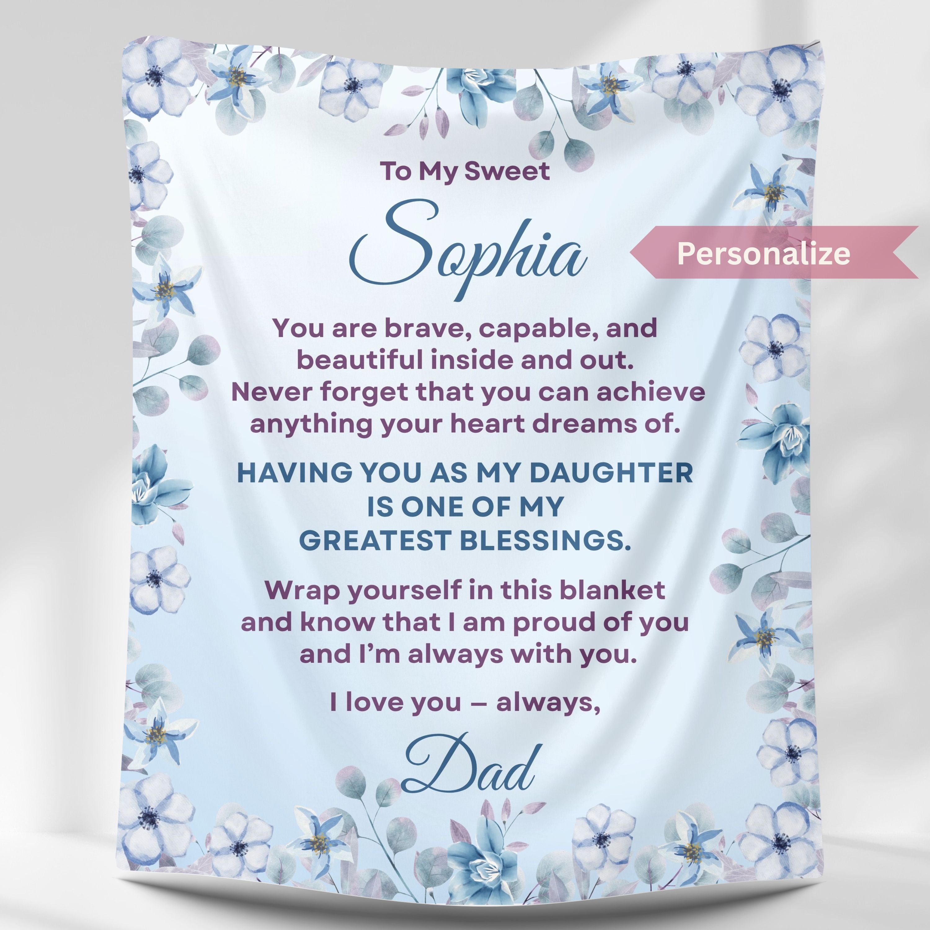 Personalized daughter blanket from Dad in cornflower with blue floral design, hanging against a white wall. 