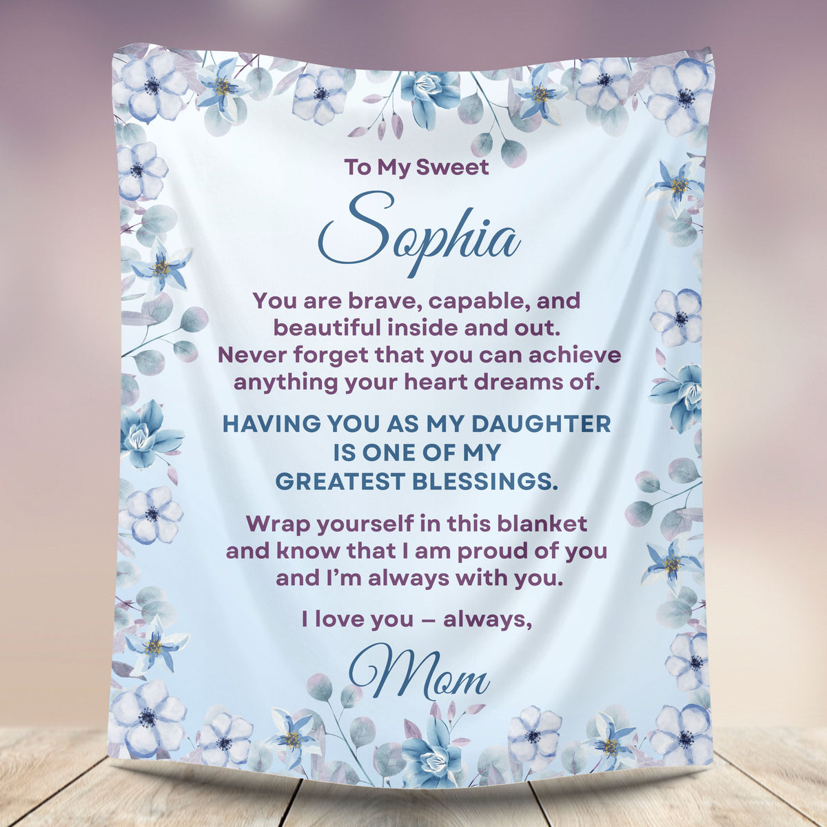 Personalized daughter blanket from Mom in Cornflower with a blue floral design, shown hanging in a cozy room setting.