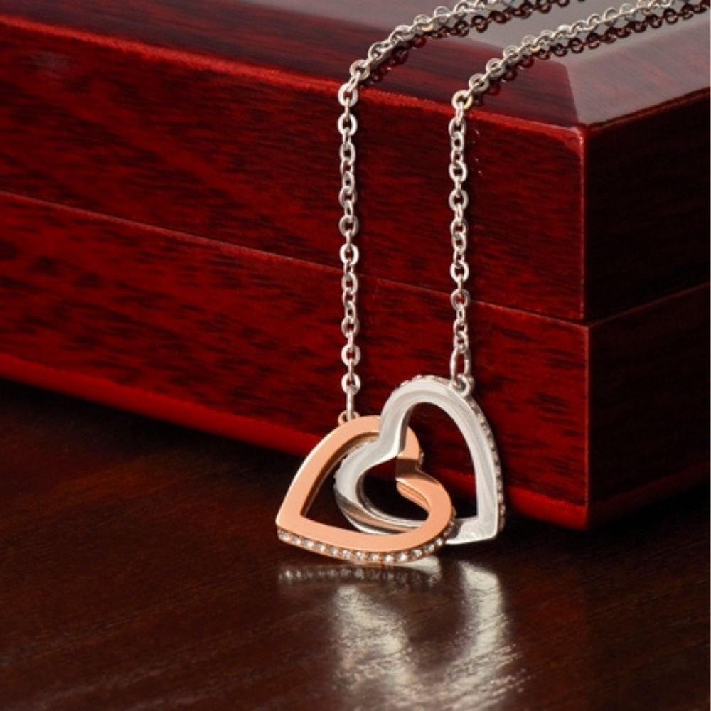 Close-up of the silver and rose gold interlocking hearts necklace resting in front of a luxury mahogany-style gift box, showcasing the pavé cubic zirconia crystals.